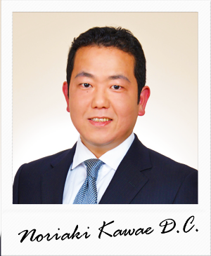 – KAWAEカイロプラクティック Professional headshot of Noriaki Kawae, D.C., smiling in a navy suit and blue tie.