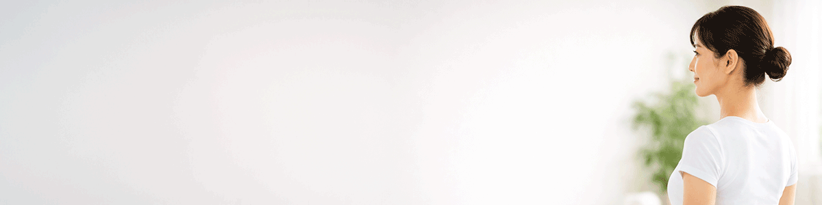 Profile of a woman with a bun in a white shirt facing left in a bright, minimalist room.